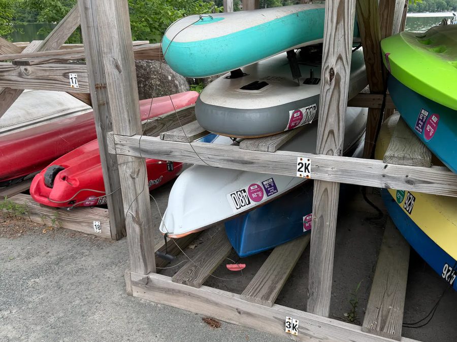 Kayaks and paddle boards stored on a wooden rack beside the lake