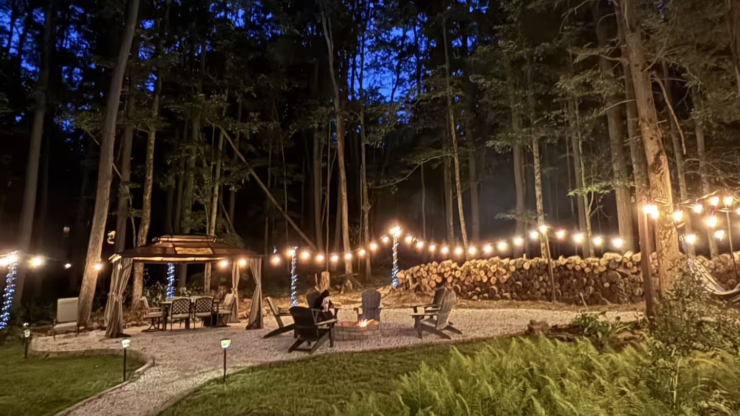 String lights strung between pine trees over the firepit area at The Lakeview at dusk